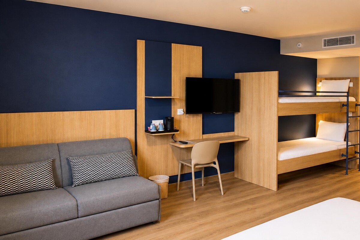 Habitación de hotel compacta con sofá, escritorio, televisión y literas.
