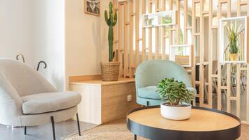 Uma sala de estar moderna com uma poltrona cinza, uma poltrona verde-água, uma mesa de centro redonda de madeira com uma planta em vaso e um painel de madeira com prateleiras.