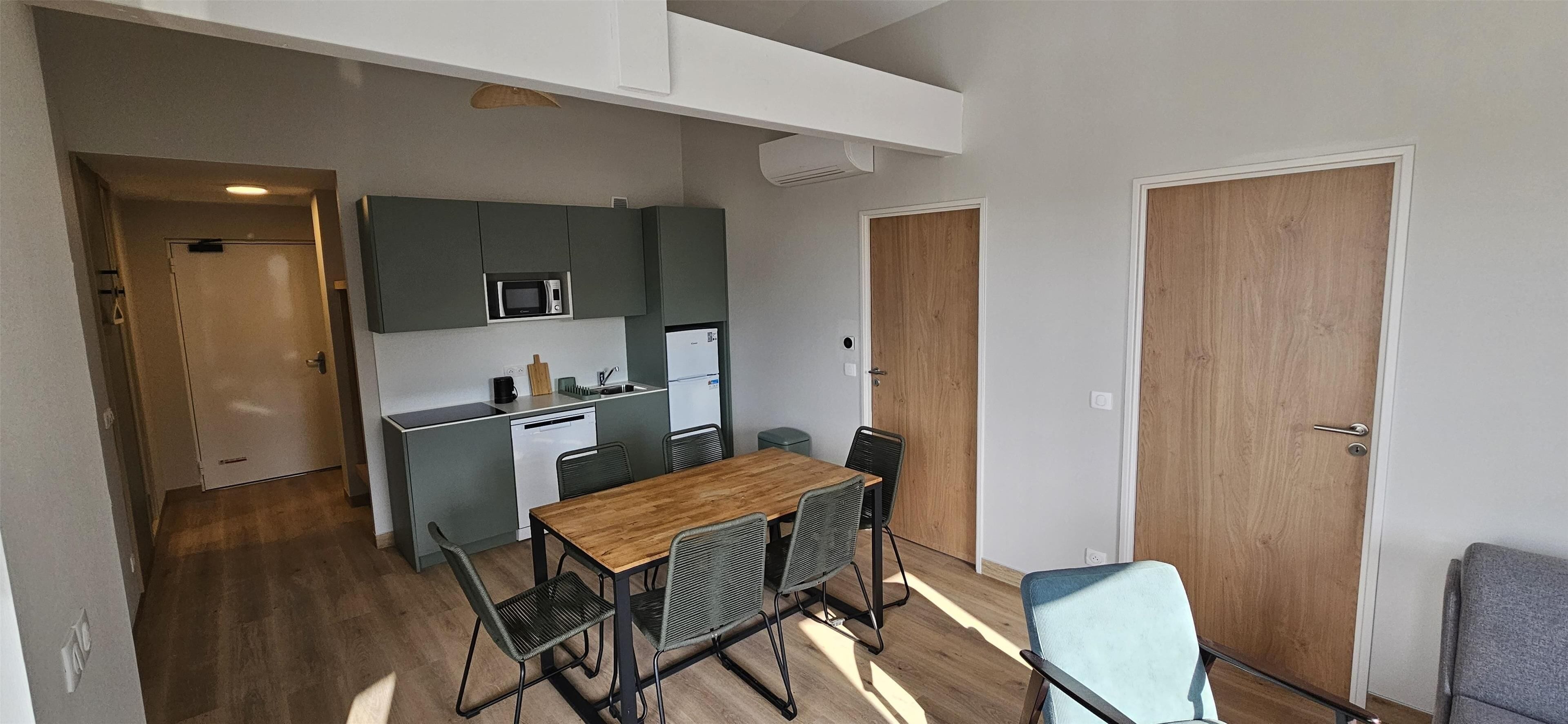 Uma cozinha compacta com uma mesa e cadeiras de madeira, micro-ondas e lava-louça.