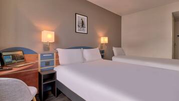 Ein Hotelzimmer mit einem Bett, einem Schreibtisch mit einem Laptop, einem Stuhl und zwei Nachttischlampen.
