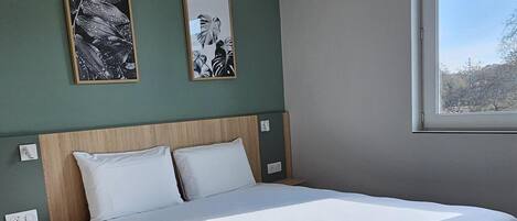A bedroom with a large bed, a hanging light fixture, and two framed pictures on the wall.