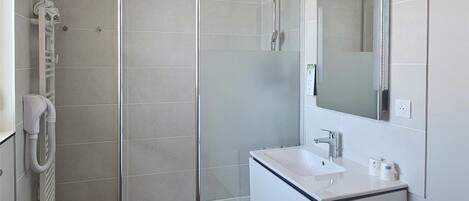A modern bathroom with a glass-enclosed shower, a built-in sink, a mirror, and a washing machine.