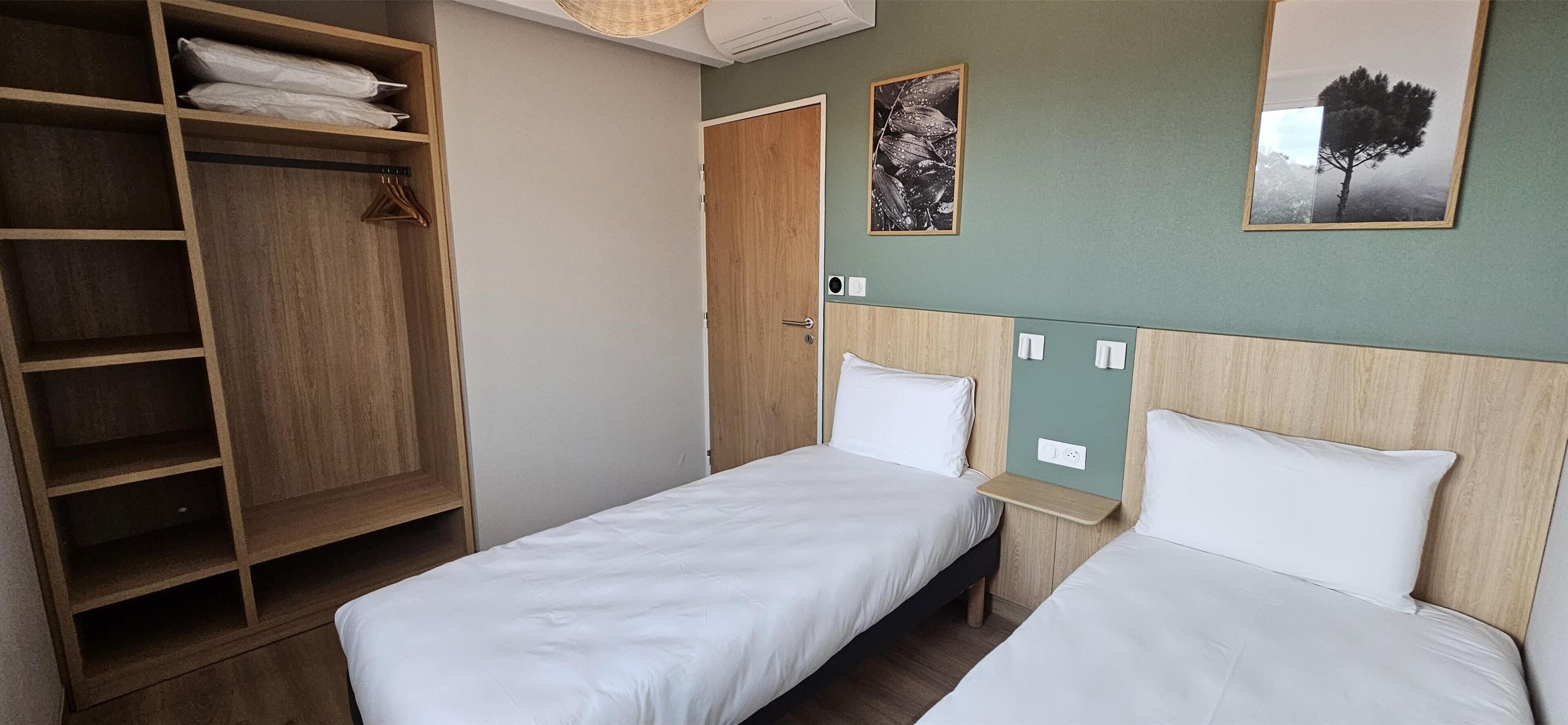Une chambre d’hôtel avec deux lits simples, une armoire en bois et une petite table de chevet.