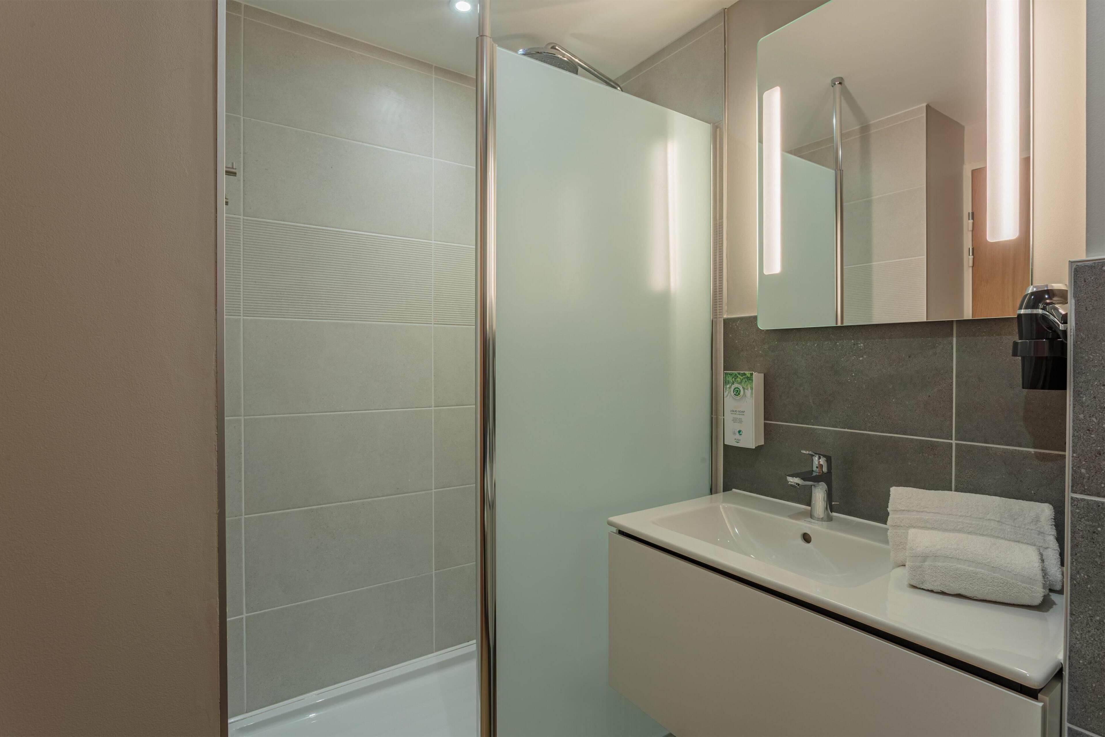Ein modernes Badezimmer mit einer Duschkabine aus Glas, einem Waschbecken mit Spiegel und einem Handtuchhalter.