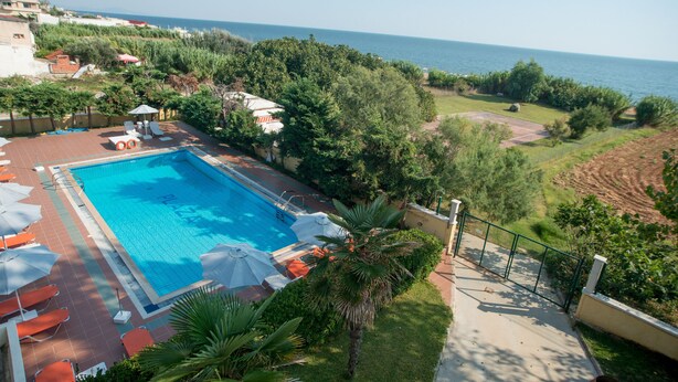 A swimming pool with lounge chairs and umbrellas, surrounded by greenery and overlooking a body of water. - Hotel Plaza (Alexandroupoli)