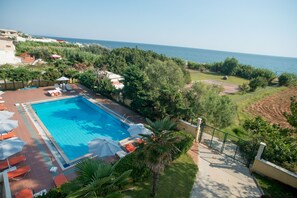 A swimming pool with lounge chairs and umbrellas, surrounded by greenery and overlooking a body of water. - Hotel Plaza (Alexandroupoli)