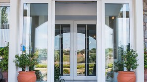 A hotel entrance with a glass door, potted plants, and a clear view of the surrounding landscape. - Hotel Plaza (Alexandroupoli)