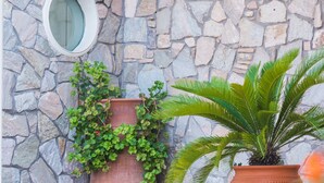 A stone wall with a circular window and two large terracotta pots with plants. - Hotel Plaza (Alexandroupoli)