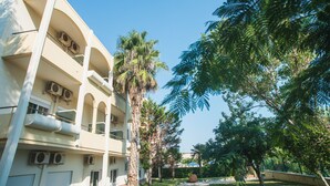 A multi-story building with balconies, air conditioning units, and a pathway leading to a palm tree-lined area. - Hotel Plaza (Alexandroupoli)