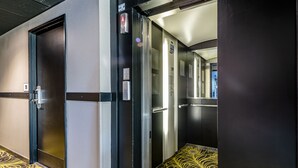 L’intérieur d’un ascenseur, avec ses portes métalliques, son panneau de commande et un tapis à motifs.