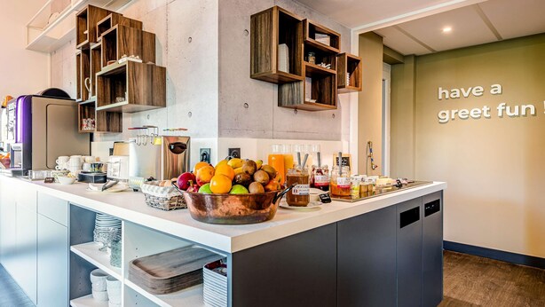 Une cuisine moderne dotée d’un îlot central où sont disposés des fruits et des boissons, de rayons en bois et un message inspirant sur le mur.