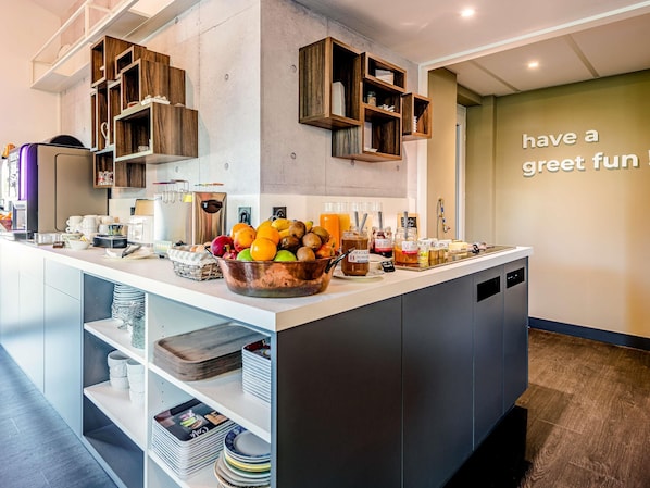 Cocina moderna con una isla central llena de frutas y bebidas, estantes de madera y un mensaje motivacional en la pared.