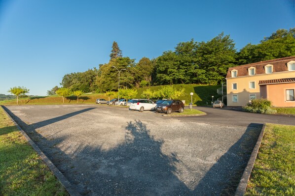 A parking lot with several cars, a building with multiple windows, and a grassy area with trees.