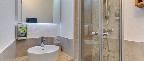 A modern bathroom with a white sink, a mirror, and a glass-enclosed shower.