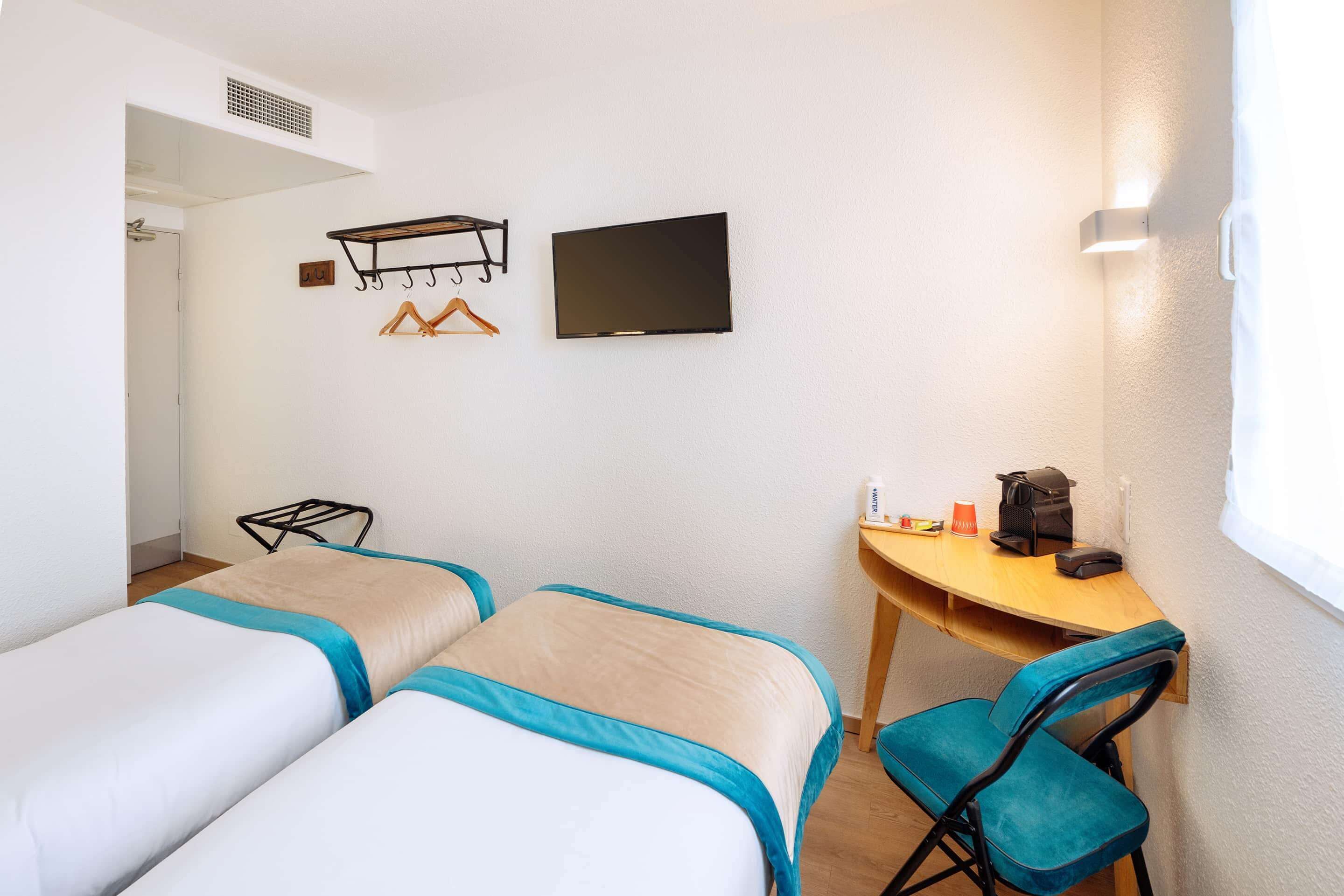 Habitación de hotel con dos camas, un escritorio, una silla, un televisor y un perchero.