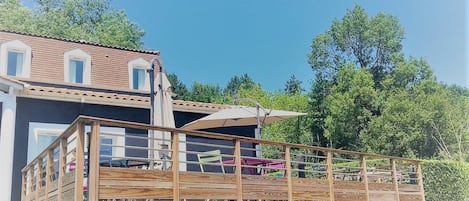 A wooden deck with a railing, a building with a tiled roof, and a clear blue sky.