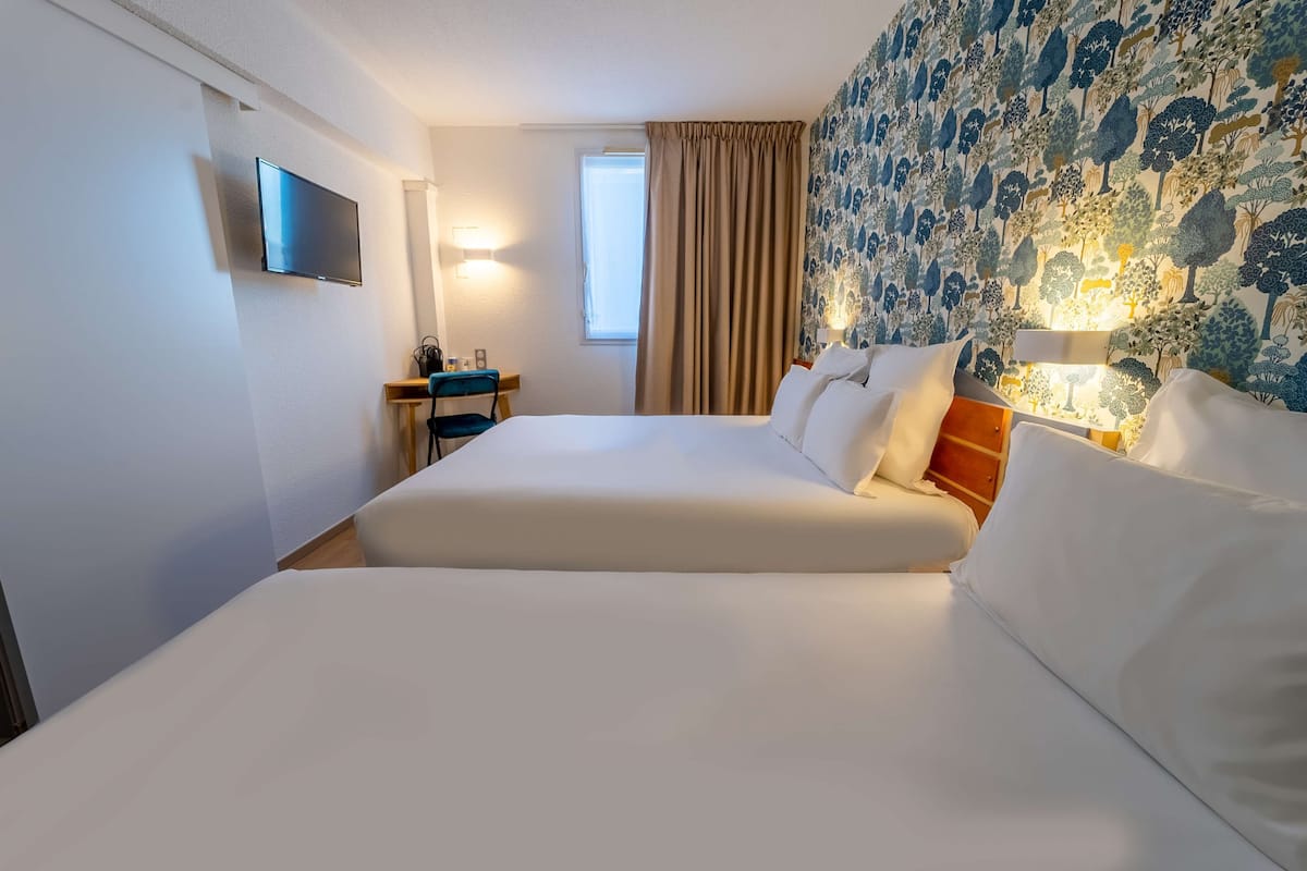 A hotel room with a large bed, a desk, a TV, and a window with curtains.
