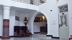 Zona de recepció amb taulell de recepció, un ample pilaret i zona d'estar amb cadires i taula.