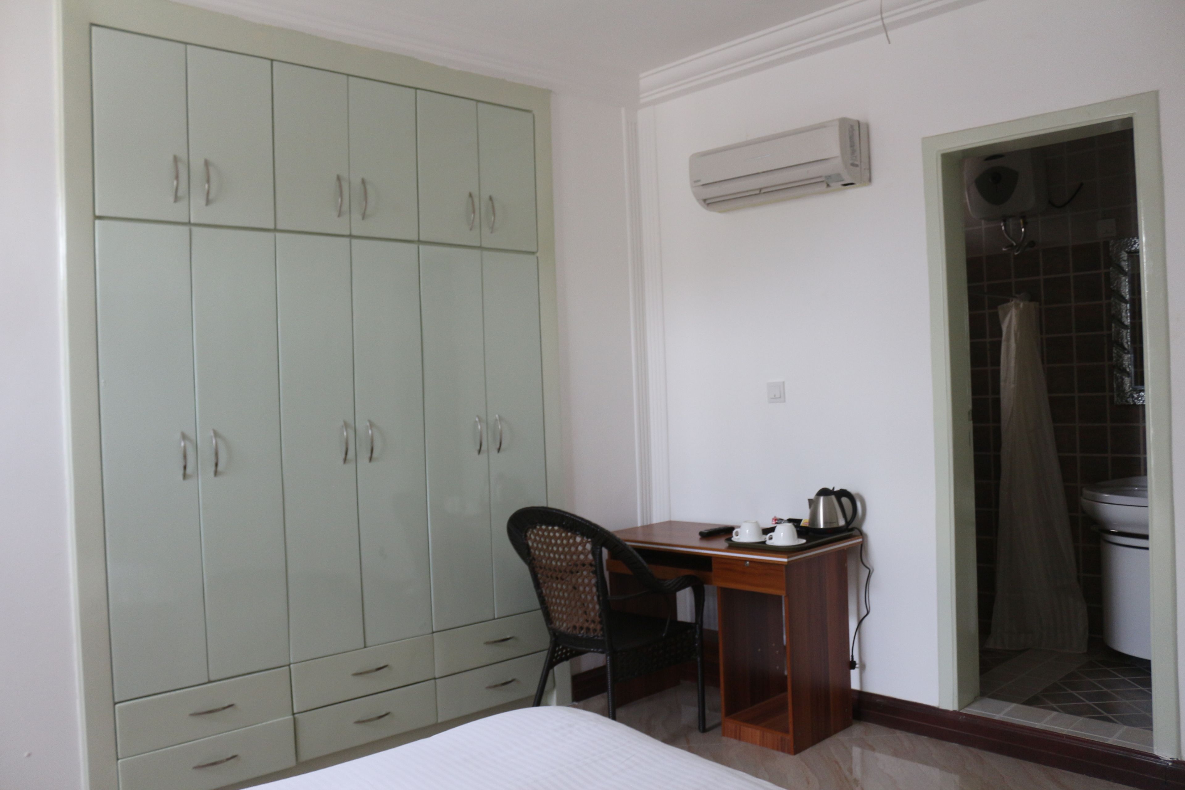 A bedroom with a bed, a desk, a chair, a wardrobe, and an air conditioning unit.