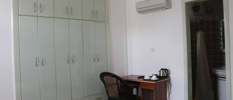 A bedroom with a bed, a desk, a chair, a wardrobe, and an air conditioning unit.