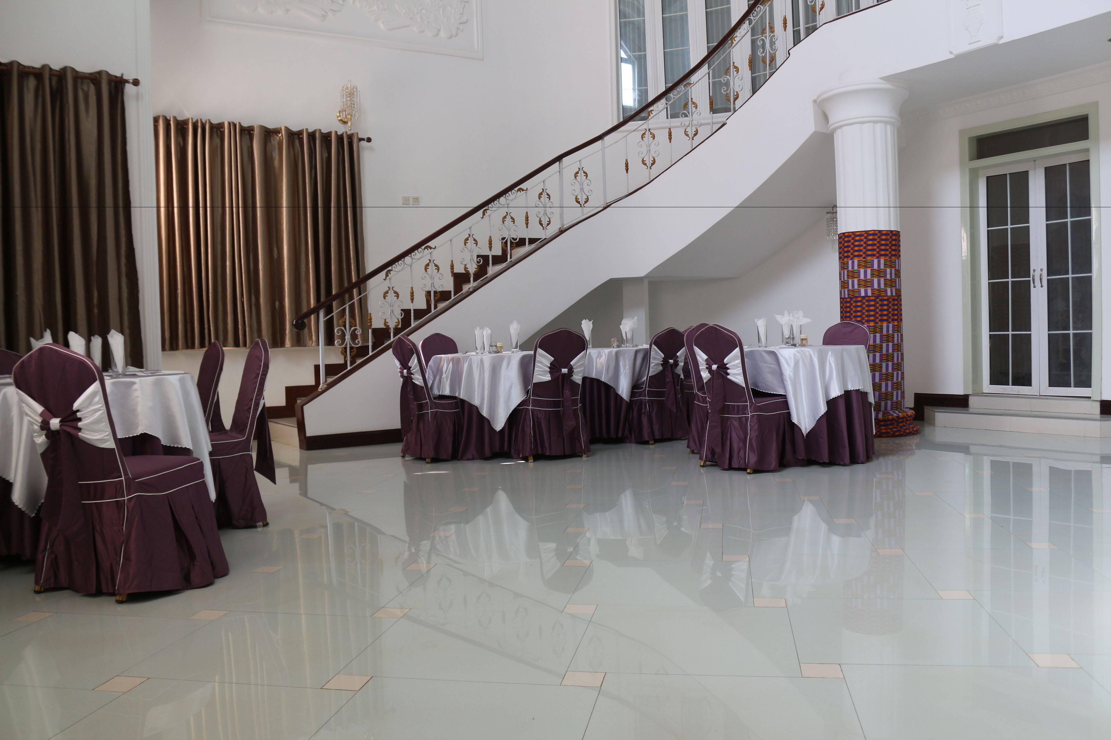 A spacious hall with a polished floor, a staircase with decorative railings, and tables set for a formal event.