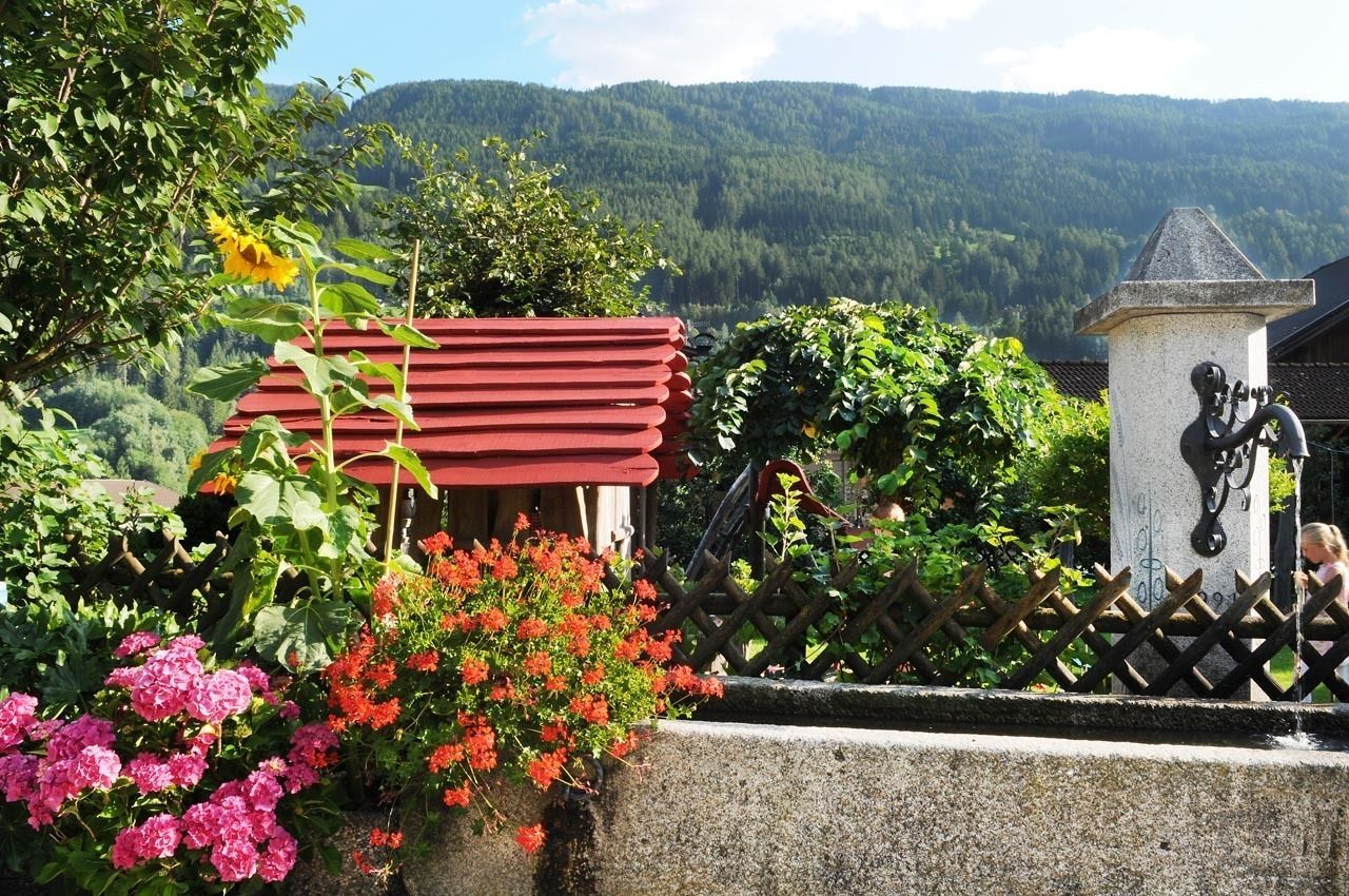 En have med en rødfarvet bygning, blomstrende planter og en statue.