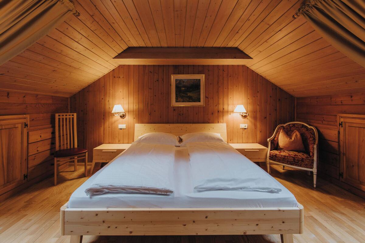 A wooden room with a bed, two nightstands, a chair, and a painting on the wall.