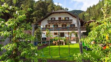 Un chalet à deux étages doté d’un balcon, entouré d’un jardin bien entretenu et bordé par une forêt.