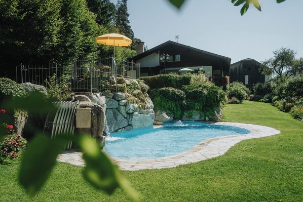 Una piscina con borda in pietra, circondata da un prato curato e una casa sullo sfondo.