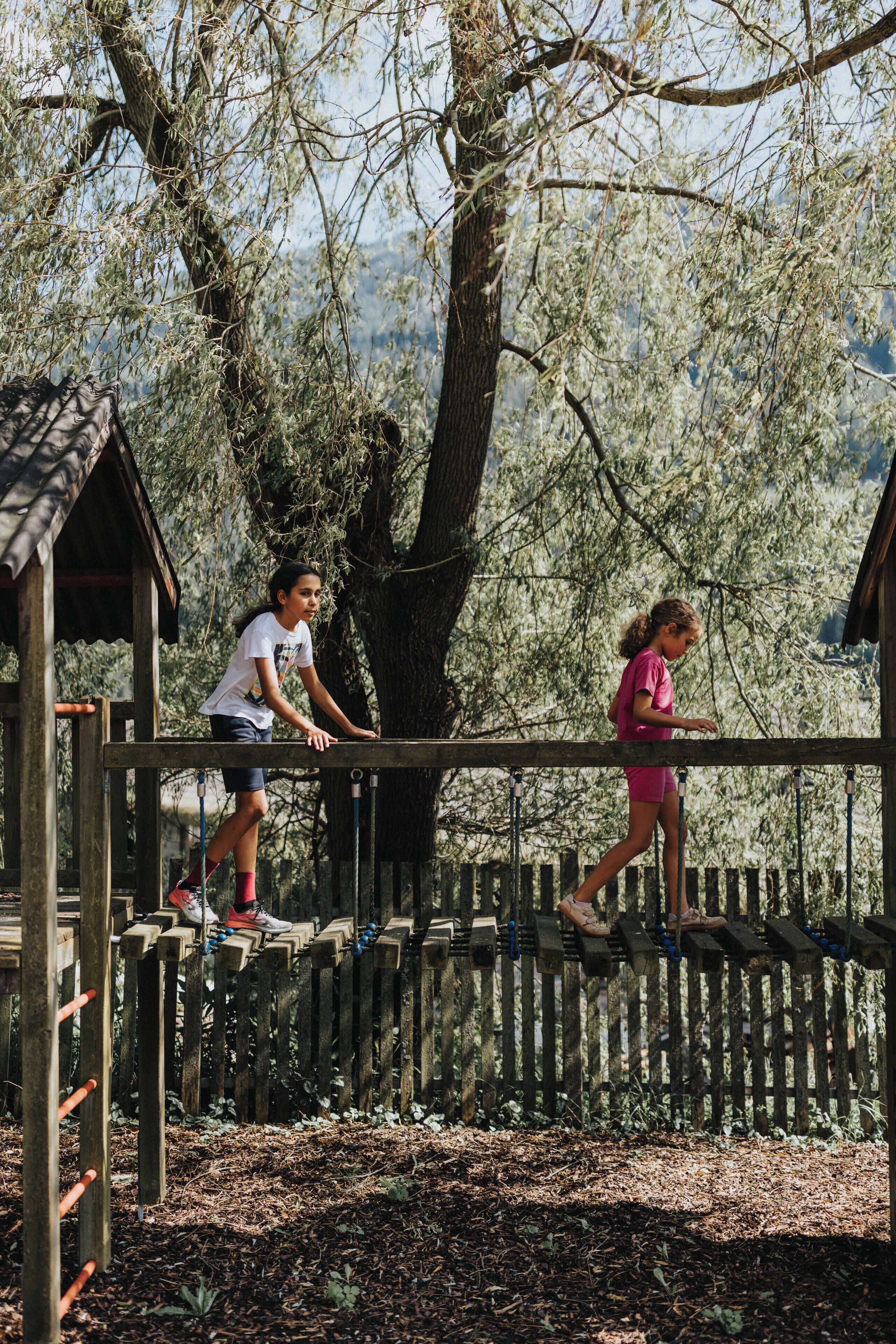 A wooden play structure with a rope bridge and a small wooden building.