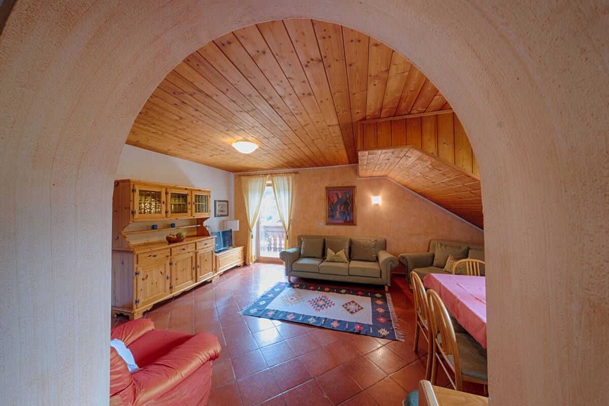 A cozy living room with a wooden ceiling, a sofa, a dining table, and a kitchen area.