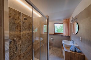 Un bagno moderno con doccia vetrata, mobile bagno in legno e un'ampia finestra che garantisce luce naturale.