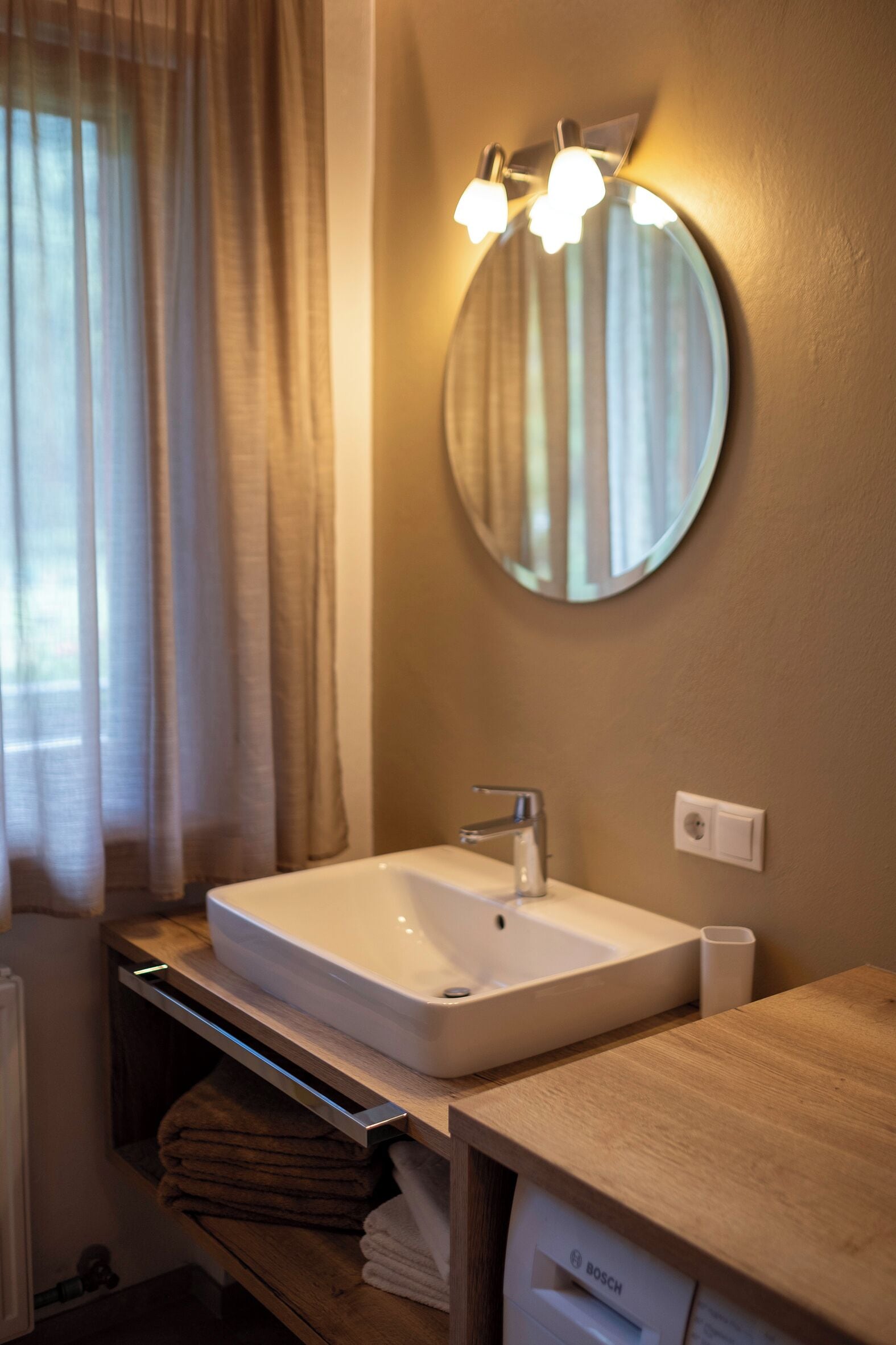 A bathroom with a white sink, a round mirror, and a wooden counter.
