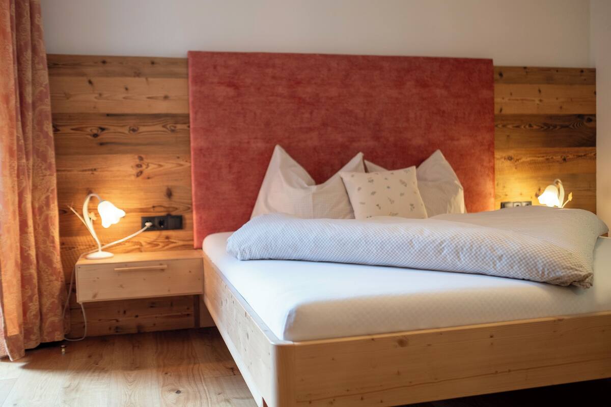 A bedroom with a wooden headboard, a bed with pillows, a nightstand with a lamp, and a wooden floor.