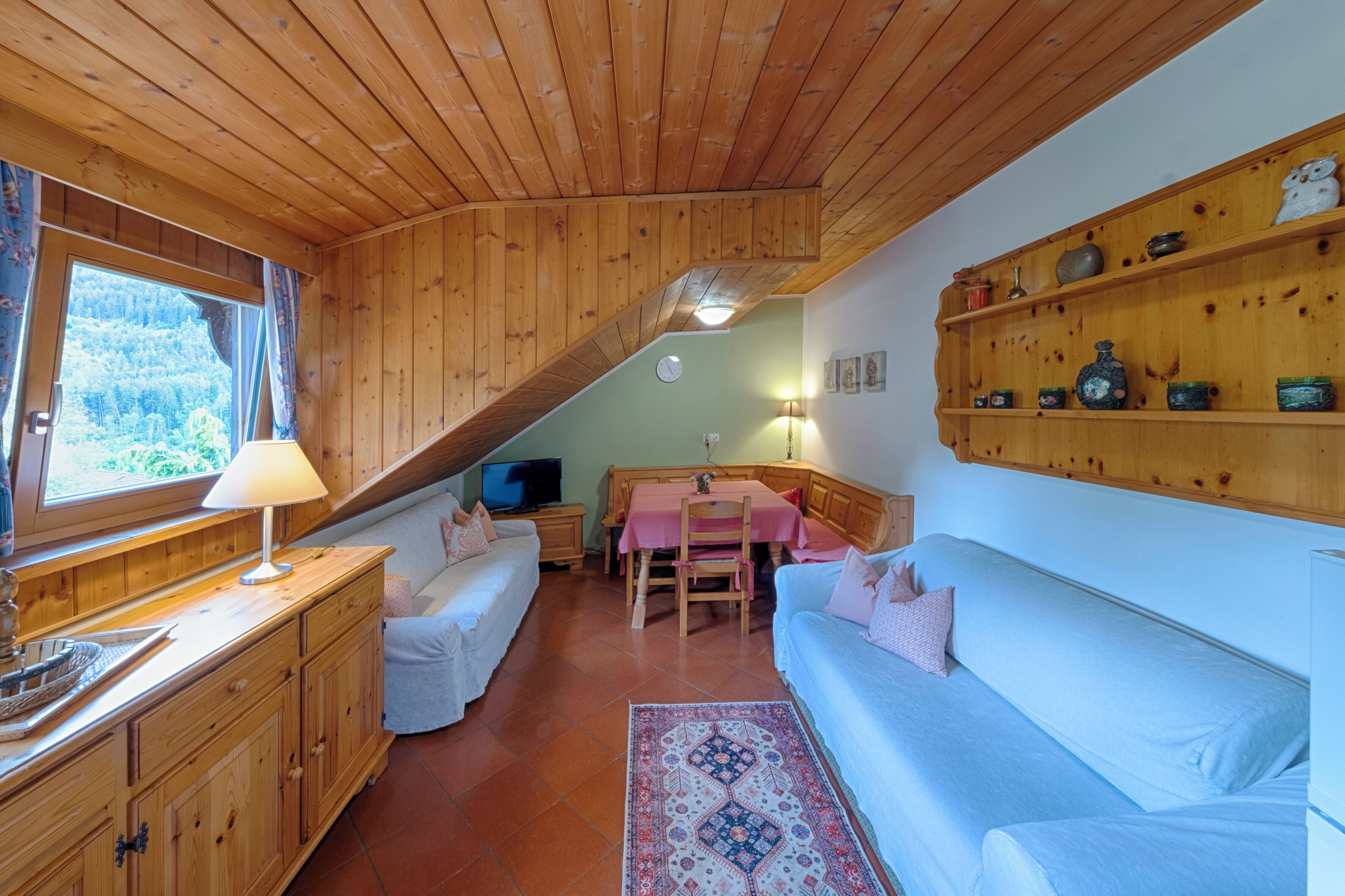 A cozy cabin interior with wooden walls, a dining area, a sofa, and a TV.