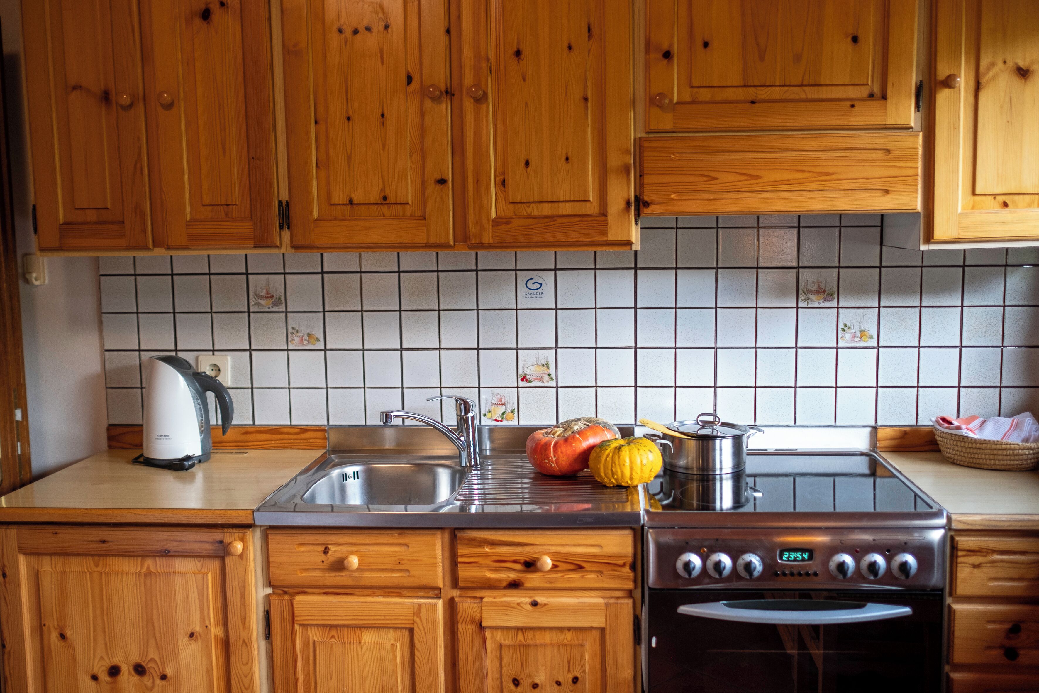 Una cocina con armarios de madera, un lavamanos de acero inoxidable, una estufa y un salpicadero de azulejos.
