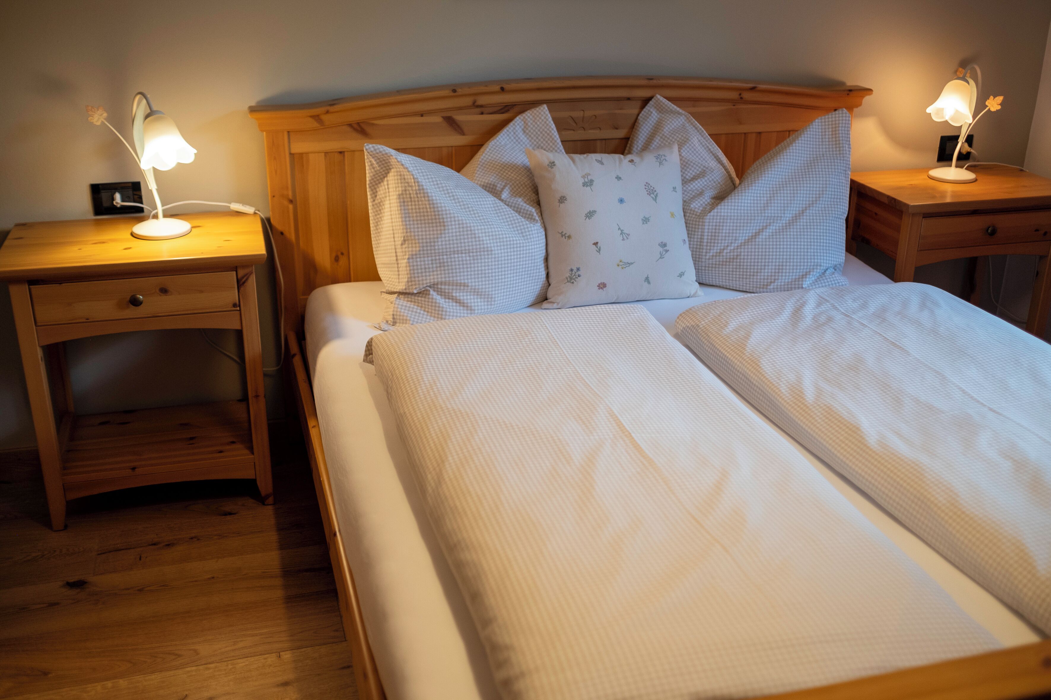 A neatly made bed with a wooden headboard, two bedside tables with lamps, and a small wooden nightstand.