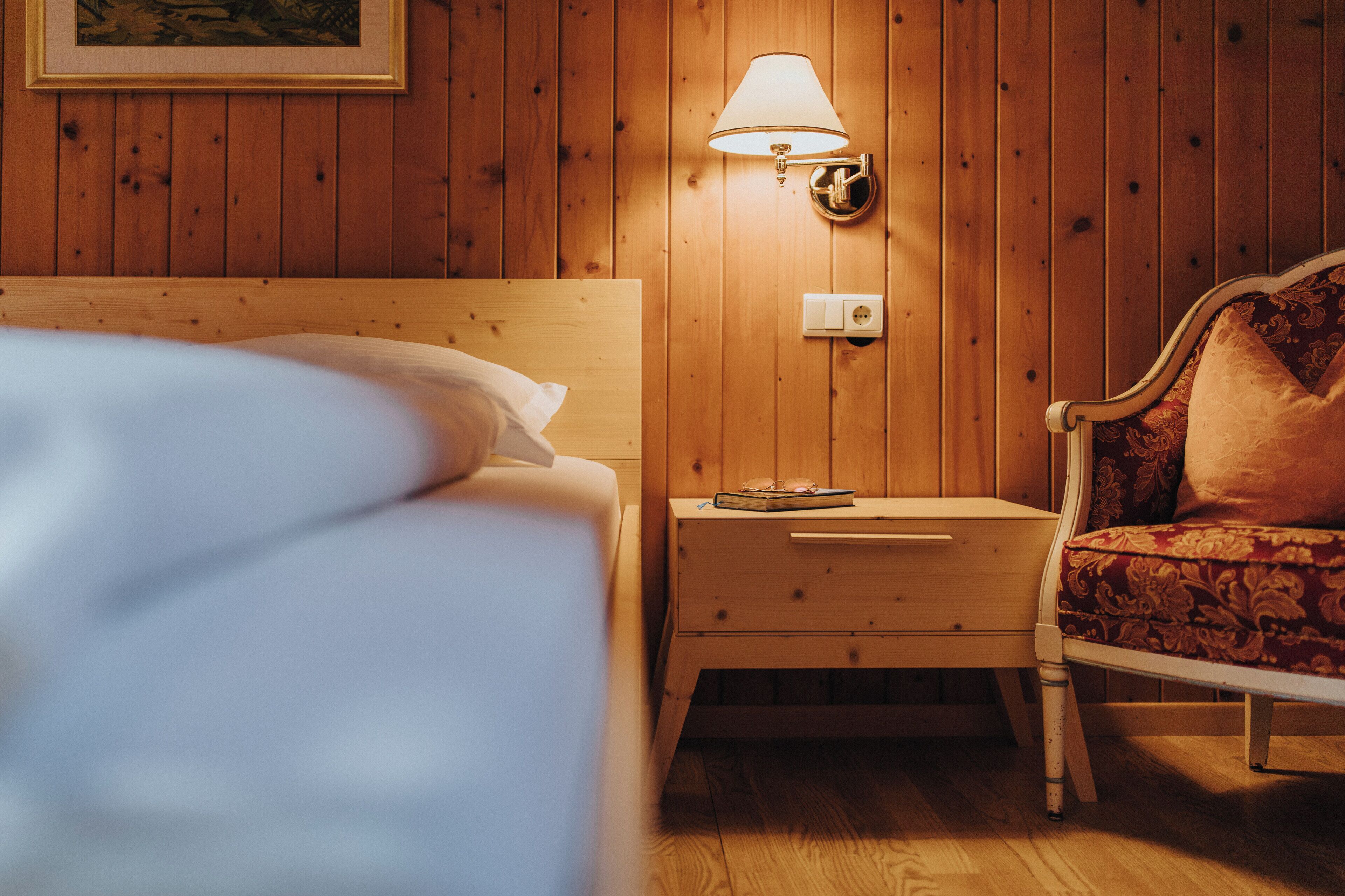 A wooden-paneled room with a bed, nightstand, lamp, and chair.