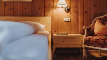 A wooden-paneled room with a bed, nightstand, lamp, and chair.