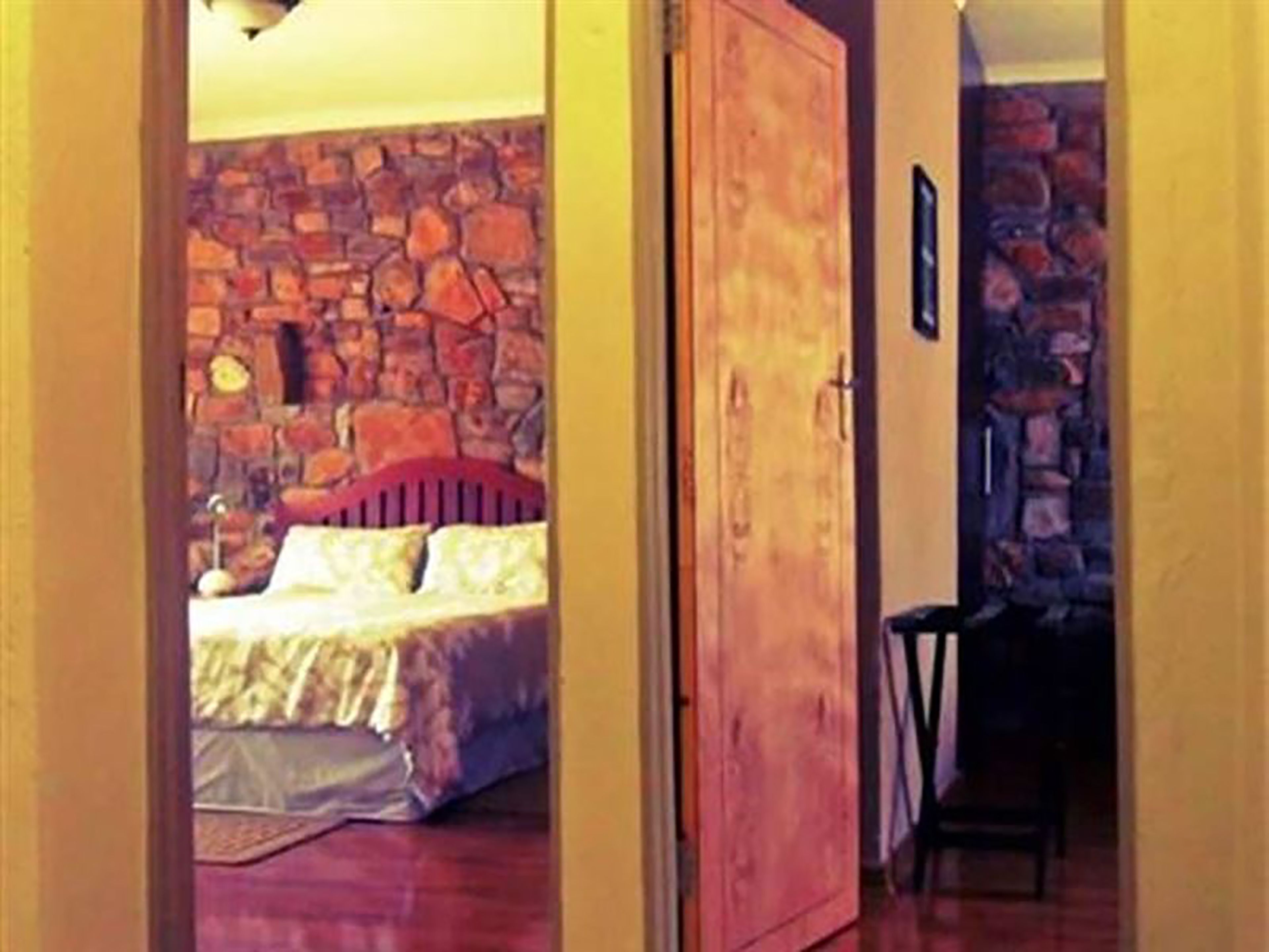 Un dormitorio con pared de piedra, puerta de madera y cama con cabecero rojo.