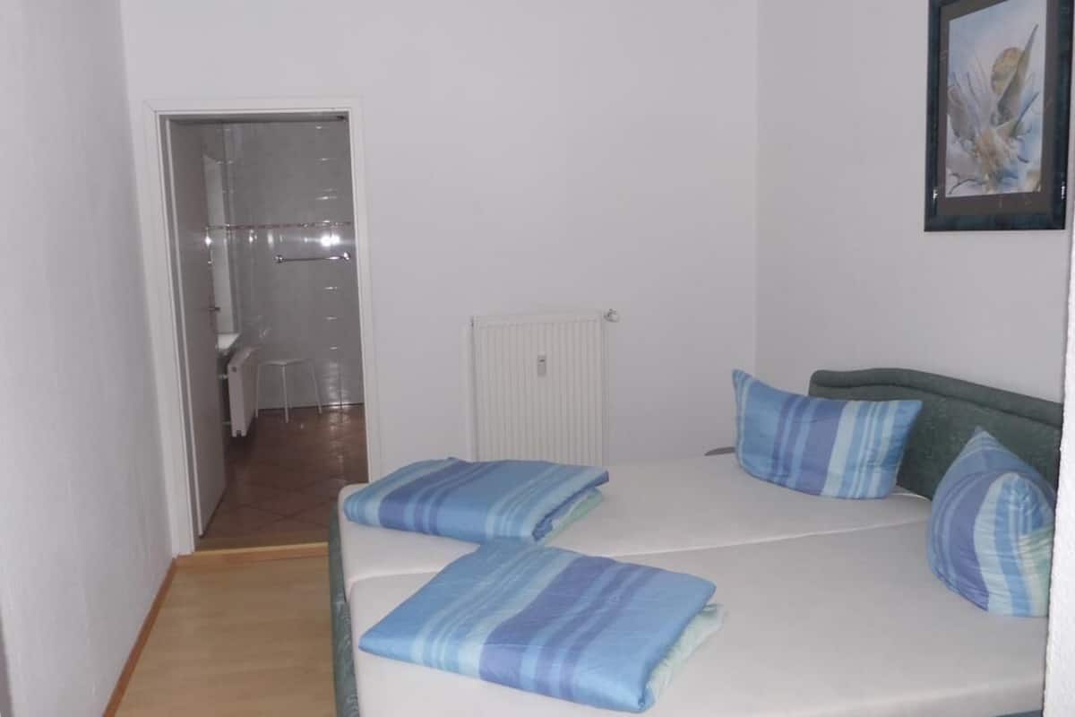 Ein kleiner, sauberer Raum mit einem Bett, einem Heizkörper und einem gerahmten Bild an der Wand.