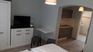 Une petite chambre comprenant un lit, un bureau, une chaise, un téléviseur et un coin cuisine.