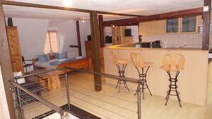 Una cocina moderna con armarios de madera y una barra. Hay una zona de comedor con sillas de mimbre y un sofá.