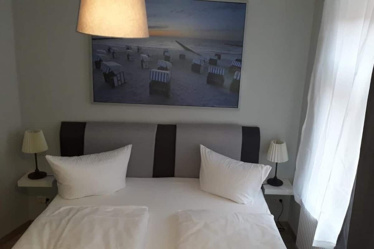 Ein Hotelzimmer mit einem großen Bett, zwei Nachttischlampen, einem Bild von Strandstühlen und einem fenster mit Vorhängen.
