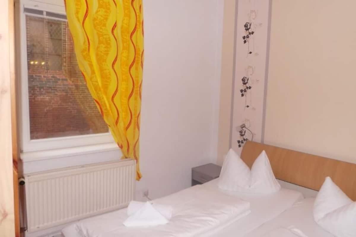 Ein Hotelzimmer mit Bett, Fenster mit Vorhang, Heizkörper und Wand mit Blumenmuster.