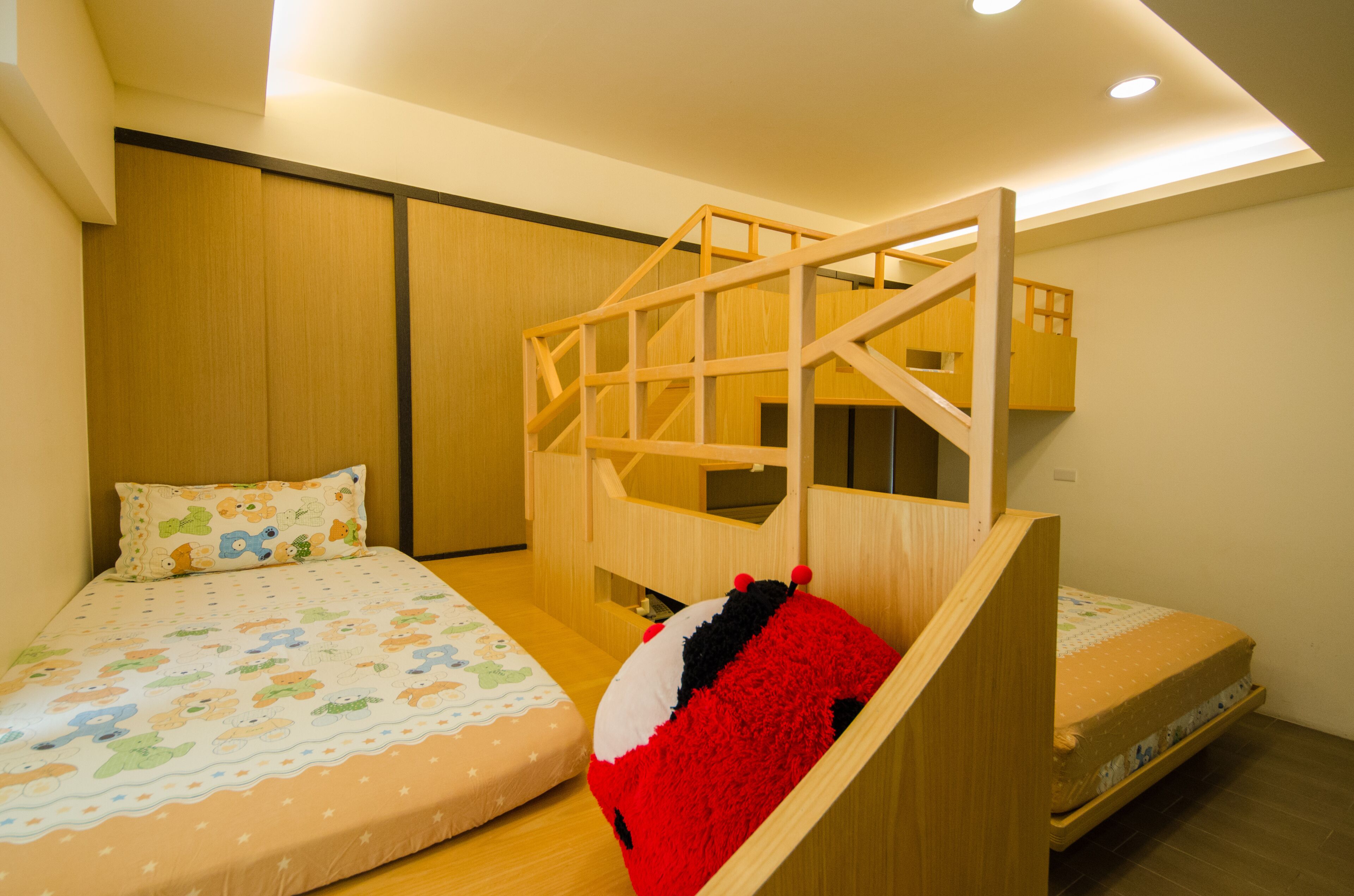 Ein Kinderzimmer mit Etagenbetten, einer Holzspielkonstellation und einem Bett mit farbenfroher Bettdecke.