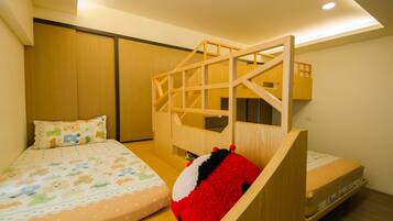 Ein Kinderzimmer mit Etagenbetten, einer Holzspielkonstellation und einem Bett mit farbenfroher Bettdecke.