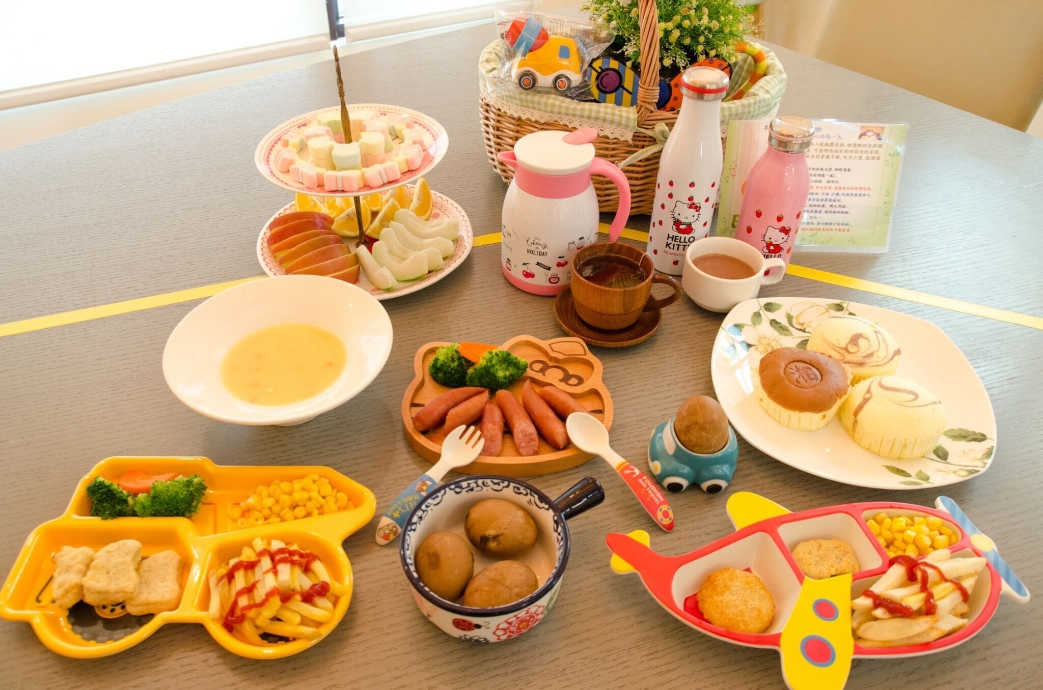Un tavolo con diversi cibi e stoviglie, tra cui piatti con cibo, una teiera e una tazza di Hello Kitty.