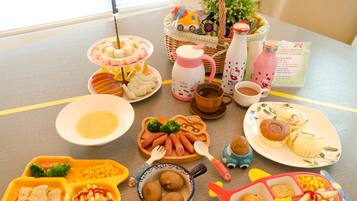Un tavolo con diversi cibi e stoviglie, tra cui piatti con cibo, una teiera e una tazza di Hello Kitty.