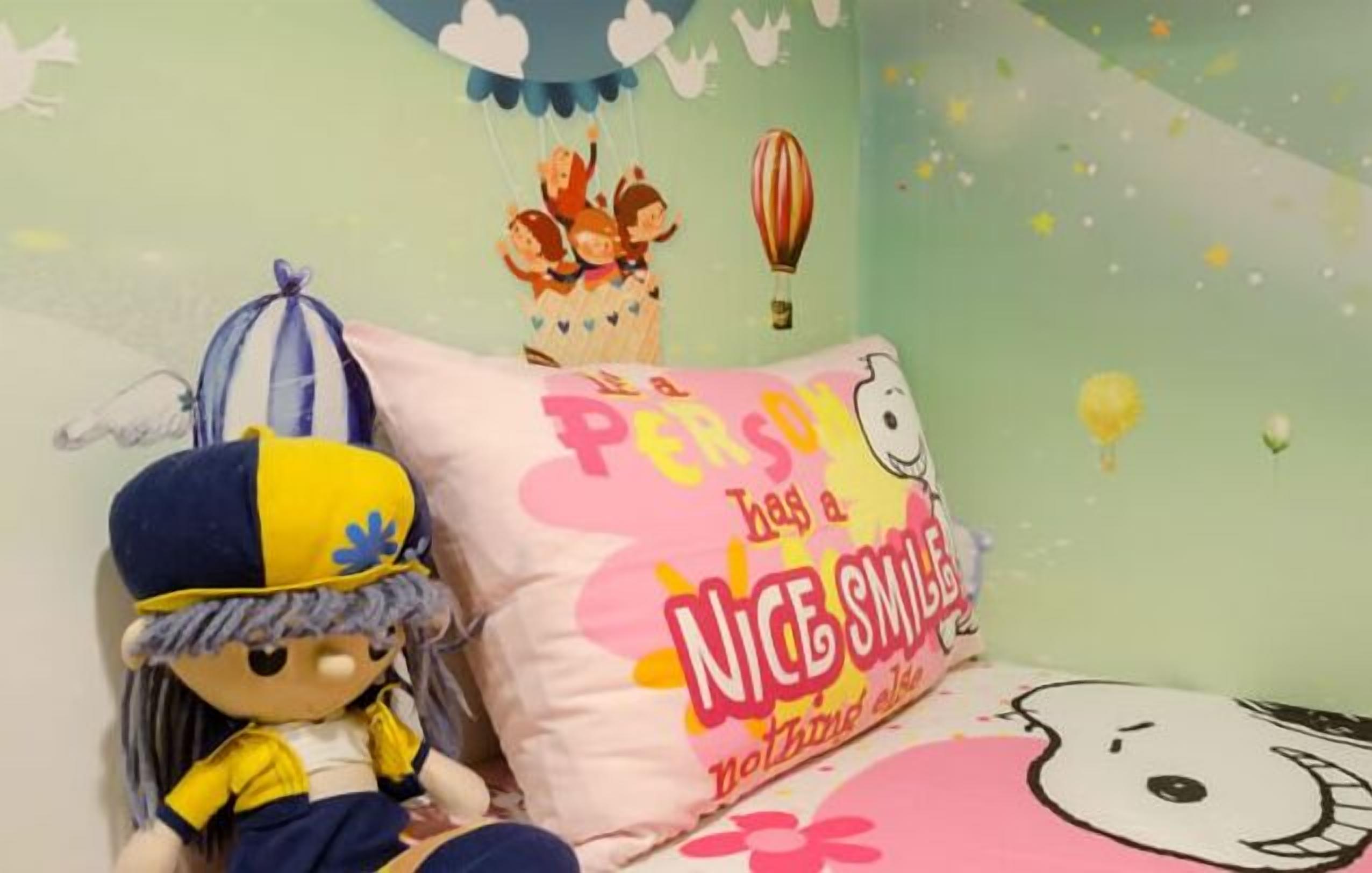 A child's room with a plush toy, a pillow with a Hello Kitty design, and a wall decorated with a hot air balloon and clouds.